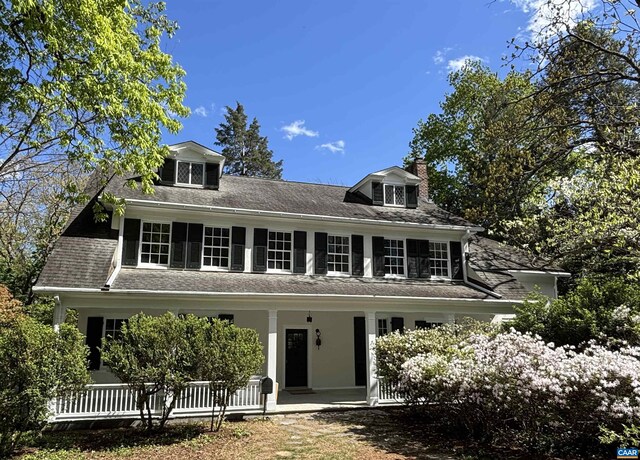view of front of property featuring a porch, a chimney, and a shingled roof