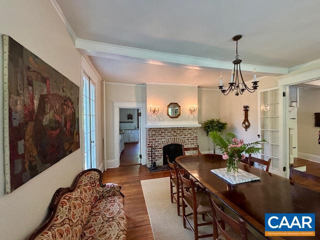 dining space with an inviting chandelier, ornamental molding, wood finished floors, a fireplace, and baseboards