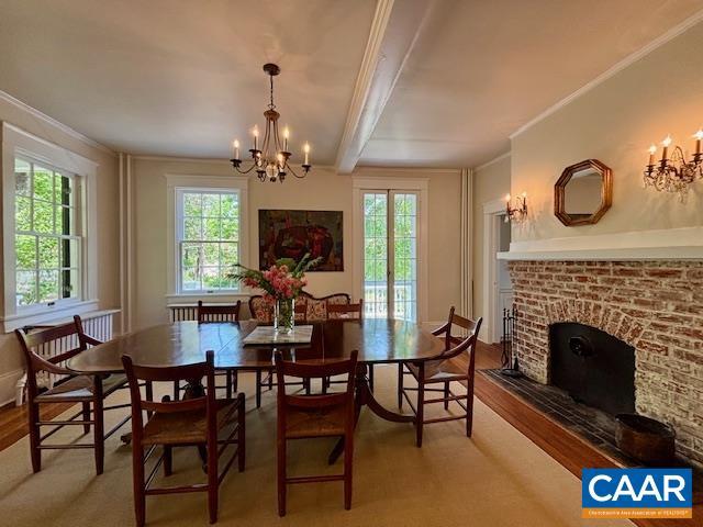 dining space with ornamental molding, a brick fireplace, wood finished floors, and a notable chandelier