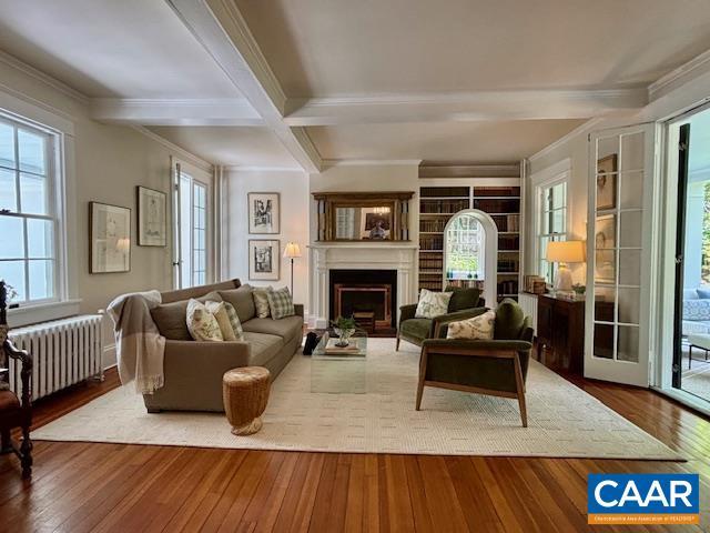 living area featuring a fireplace, beamed ceiling, wood-type flooring, radiator, and ornamental molding