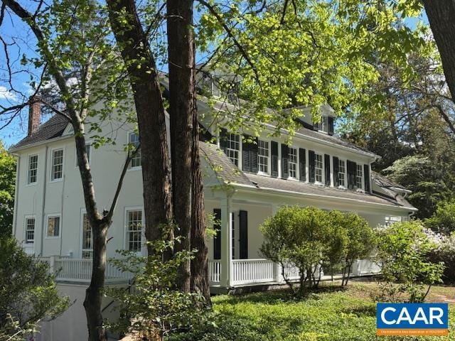 back of house with covered porch, a chimney, and stucco siding