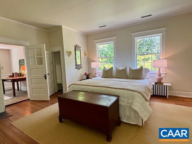 bedroom with baseboards, ornamental molding, wood finished floors, and visible vents