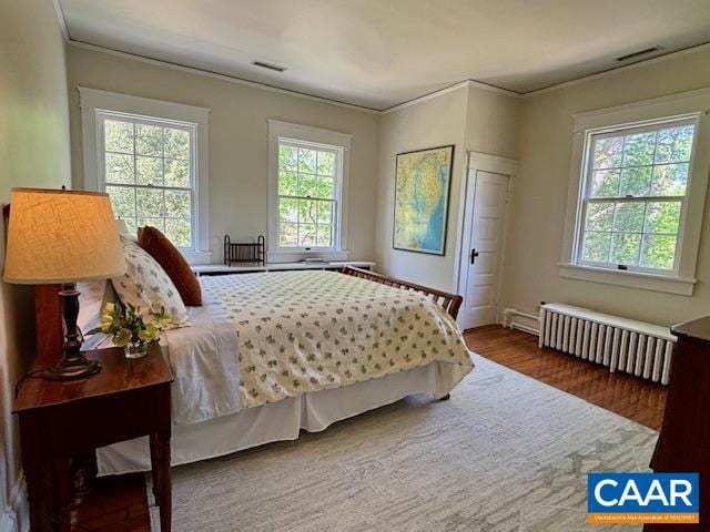 bedroom featuring crown molding, radiator, wood finished floors, and visible vents