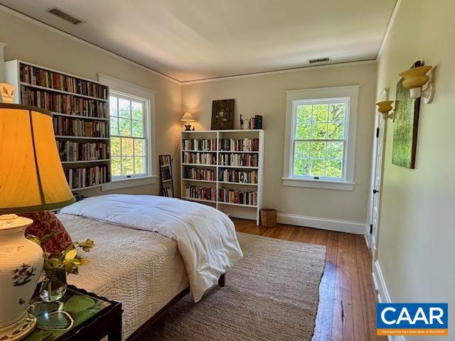 bedroom with crown molding, baseboards, visible vents, and hardwood / wood-style floors