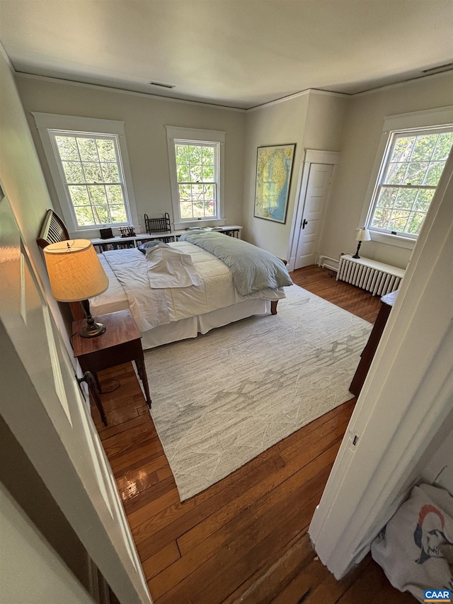 bedroom with radiator heating unit, wood finished floors, and visible vents