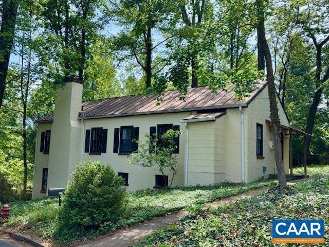 view of side of home with stucco siding, metal roof, a chimney, and a standing seam roof