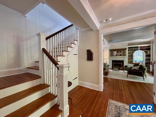 staircase featuring wood-type flooring, ornamental molding, baseboards, and a fireplace