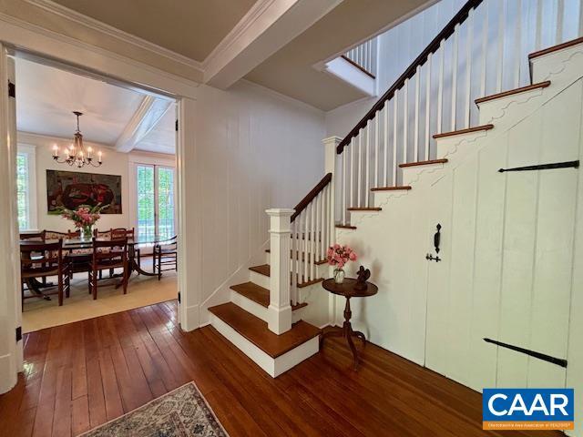 staircase featuring crown molding, beamed ceiling, a chandelier, and hardwood / wood-style flooring