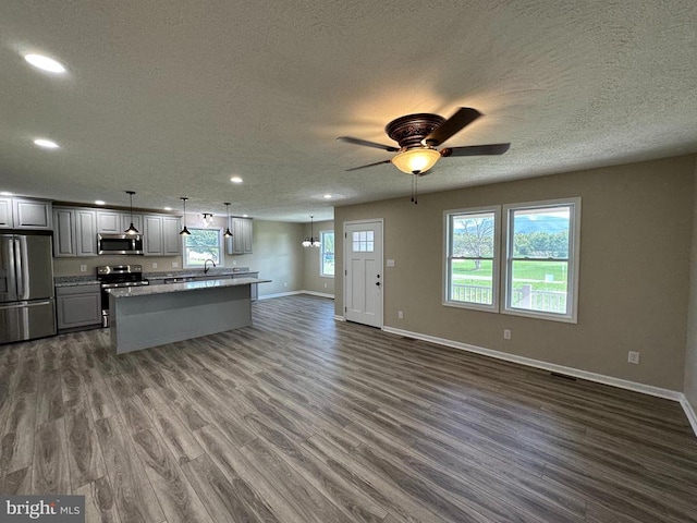 kitchen featuring dark wood-type flooring, appliances with stainless steel finishes, gray cabinets, ceiling fan, and hanging light fixtures