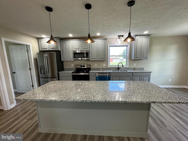 kitchen featuring gray cabinets, a kitchen island, stainless steel appliances, dark wood-type flooring, and decorative light fixtures