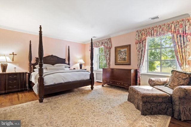 bedroom with radiator heating unit, wood-type flooring, crown molding, and multiple windows