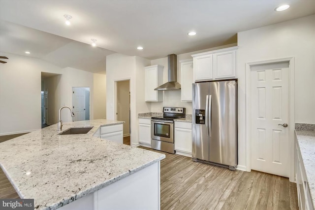 kitchen featuring an island with sink, stainless steel appliances, wall chimney exhaust hood, light stone counters, and sink