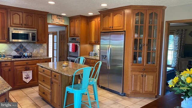 kitchen featuring light tile patterned flooring, tasteful backsplash, stainless steel appliances, light stone counters, and a kitchen island