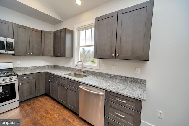 kitchen with sink, stainless steel appliances, light stone counters, dark brown cabinetry, and dark hardwood / wood-style flooring