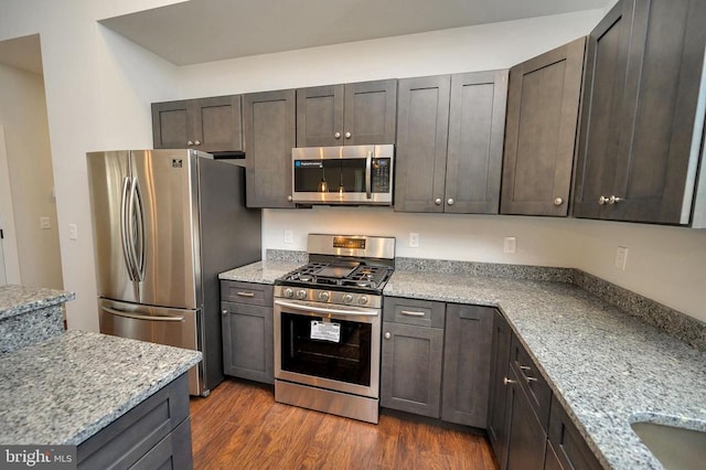 kitchen with dark brown cabinets, appliances with stainless steel finishes, dark hardwood / wood-style floors, and light stone countertops