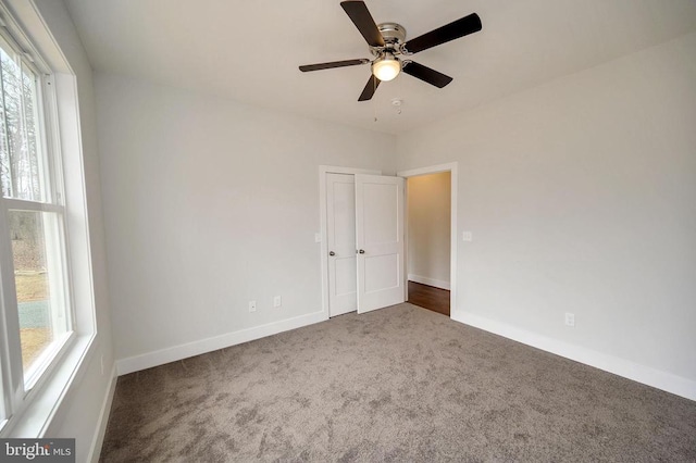 spare room featuring a healthy amount of sunlight, dark colored carpet, and ceiling fan