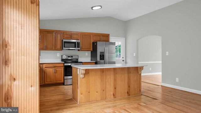 kitchen with appliances with stainless steel finishes, light wood-type flooring, a kitchen island, and a kitchen bar