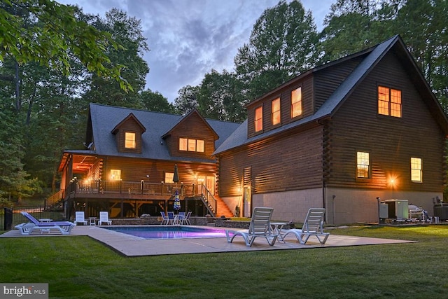 back house at dusk with a patio, a swimming pool side deck, central air condition unit, and a yard