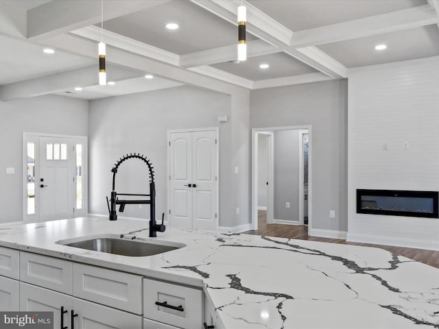 kitchen featuring pendant lighting, white cabinets, sink, light stone countertops, and beamed ceiling