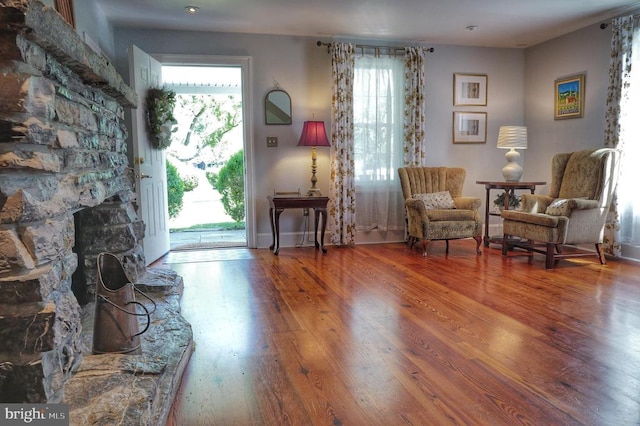 sitting room featuring a stone fireplace, hardwood / wood-style floors, and a healthy amount of sunlight