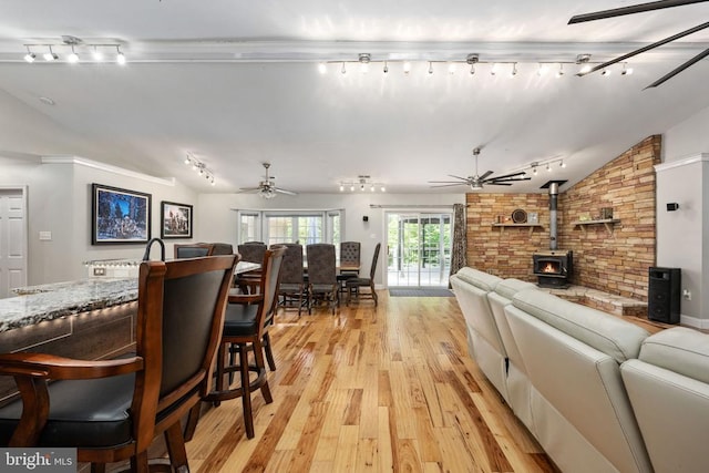 living room featuring lofted ceiling, ceiling fan, a wood stove, and light hardwood / wood-style flooring