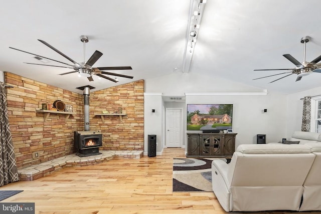 living room featuring a wood stove, ceiling fan, light hardwood / wood-style flooring, and vaulted ceiling