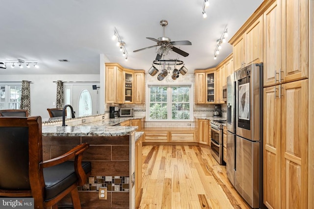 kitchen with kitchen peninsula, appliances with stainless steel finishes, decorative backsplash, light stone counters, and light hardwood / wood-style flooring