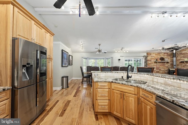 kitchen featuring a wood stove, sink, stainless steel appliances, light stone counters, and light hardwood / wood-style flooring