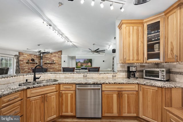 kitchen featuring kitchen peninsula, backsplash, light stone counters, vaulted ceiling, and sink