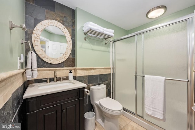 bathroom with vanity, a shower with door, tile patterned floors, toilet, and tile walls