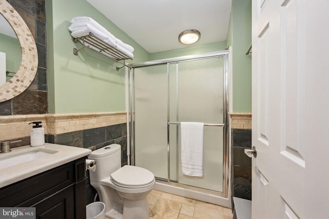 bathroom featuring walk in shower, vanity, toilet, and tile walls