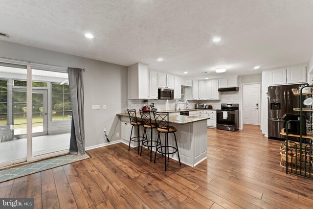 kitchen with white cabinets, kitchen peninsula, refrigerator with ice dispenser, electric range, and wood-type flooring