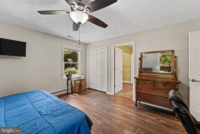 bedroom featuring a closet, hardwood / wood-style floors, a textured ceiling, a baseboard radiator, and ceiling fan