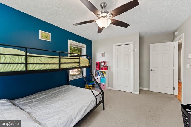 carpeted bedroom featuring ceiling fan, a closet, and a textured ceiling