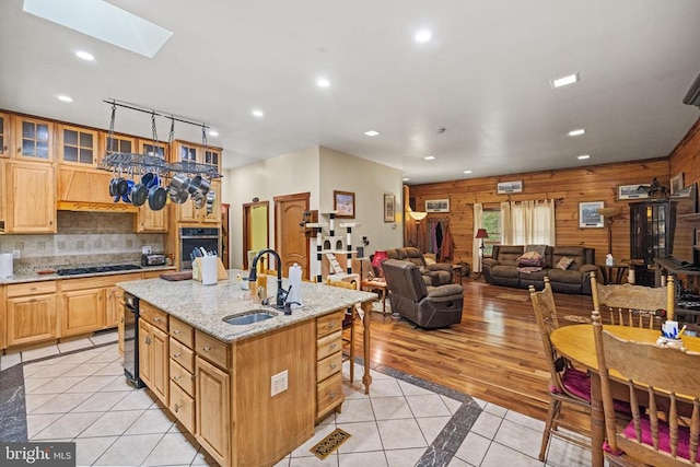 kitchen with a skylight, wooden walls, light tile patterned floors, and a center island with sink