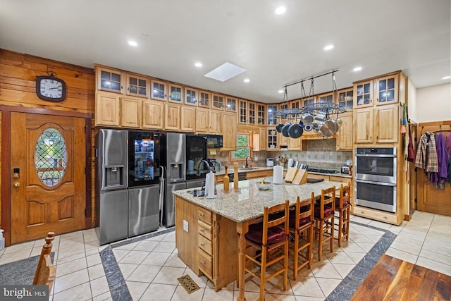 kitchen featuring a breakfast bar, light tile patterned floors, stainless steel appliances, light stone countertops, and a center island with sink