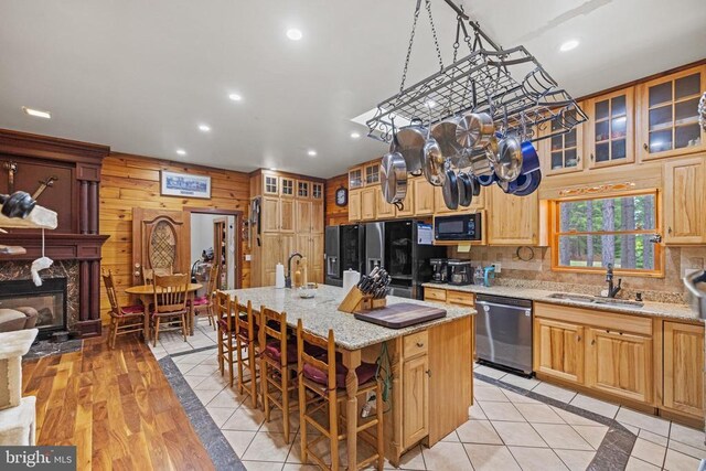 kitchen featuring black appliances, sink, a kitchen island with sink, light wood-type flooring, and light stone countertops