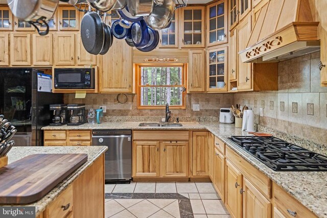 kitchen featuring tasteful backsplash, light stone countertops, black appliances, custom exhaust hood, and sink