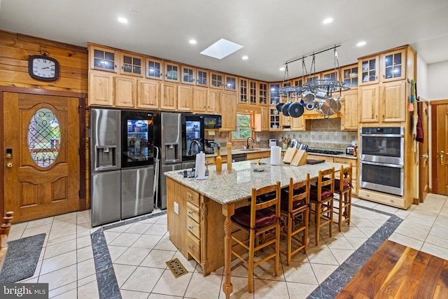 kitchen featuring light tile patterned flooring, a breakfast bar area, an island with sink, light stone countertops, and appliances with stainless steel finishes