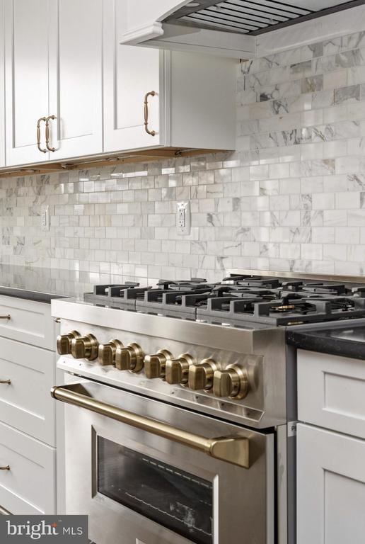 kitchen with stainless steel stove, exhaust hood, white cabinetry, and backsplash