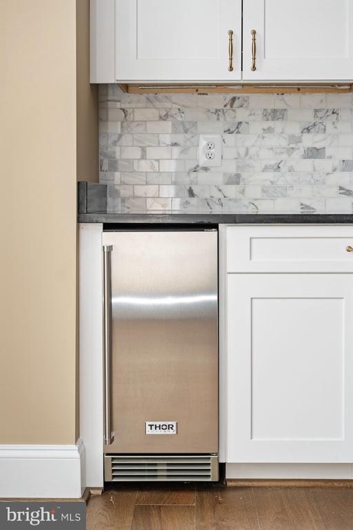 bar featuring dark wood-type flooring, white cabinetry, built in refrigerator, and tasteful backsplash