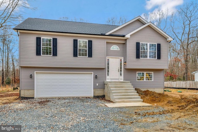 bi-level home with driveway, a shingled roof, a garage, and fence