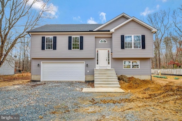 split foyer home featuring driveway, an attached garage, fence, and a shingled roof