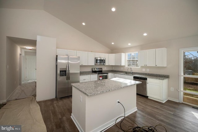 kitchen with light stone counters, stainless steel appliances, a kitchen island, a sink, and white cabinetry