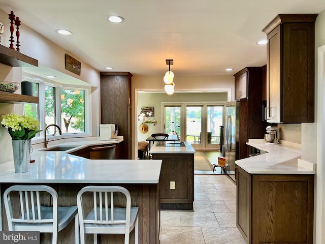 kitchen with decorative light fixtures, stainless steel appliances, dark brown cabinetry, sink, and kitchen peninsula