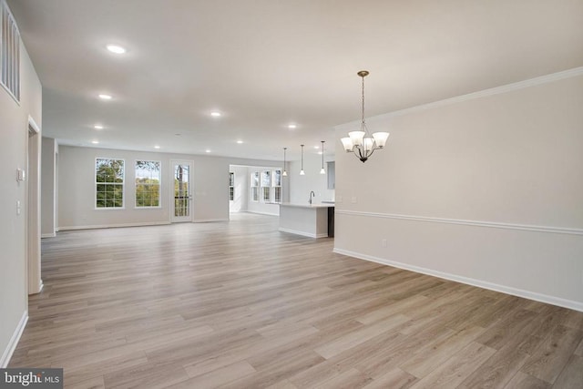 unfurnished living room featuring an inviting chandelier, ornamental molding, sink, and light hardwood / wood-style floors