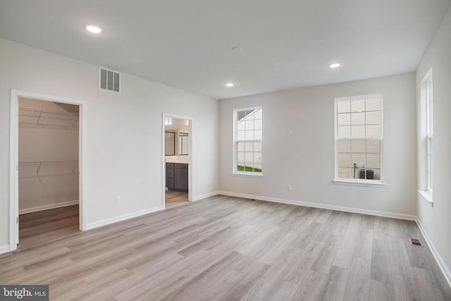 unfurnished bedroom with a closet, a walk in closet, ensuite bath, and light wood-type flooring