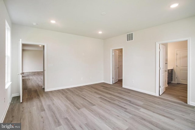 unfurnished bedroom featuring a closet, a spacious closet, ensuite bath, and light wood-type flooring