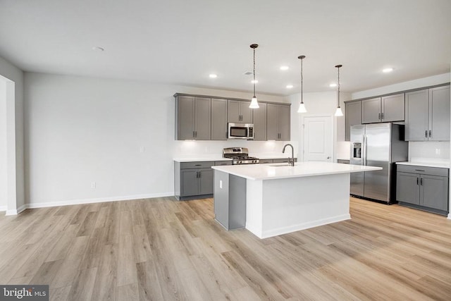 kitchen with a kitchen island with sink, stainless steel appliances, decorative light fixtures, gray cabinets, and light hardwood / wood-style floors