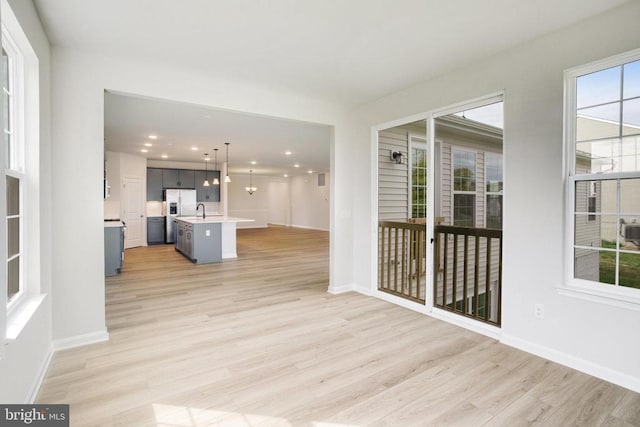 interior space with light hardwood / wood-style flooring, a wealth of natural light, an island with sink, and hanging light fixtures